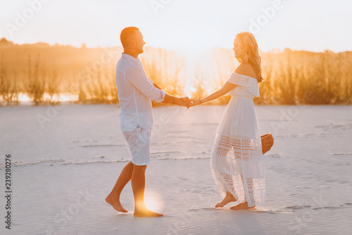 A bearded man and a blond woman are embraced and illuminated by a sunbeam. Closeup portrait of emotional people at sunset. Love in the desert newlyweds. The love story of merry and lovers young.