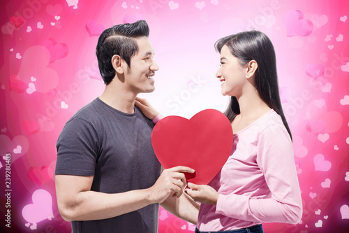 Young asian couple holding red heart shape and looking at one another