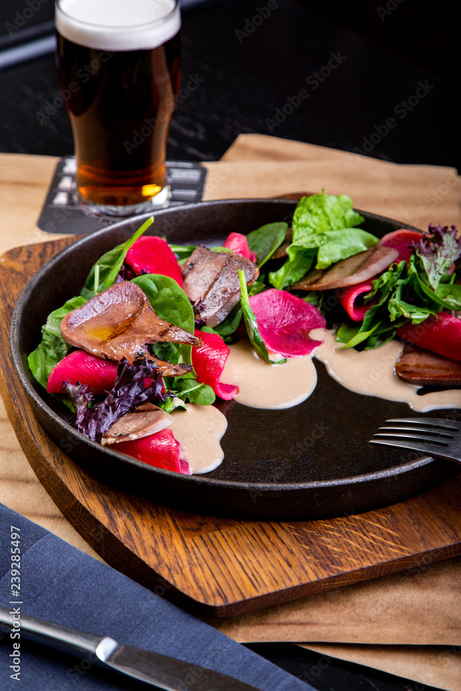 delicious beef tongue with spinach and beetroot in restaurant background. Healthy exclusive food on big black platter closeup
