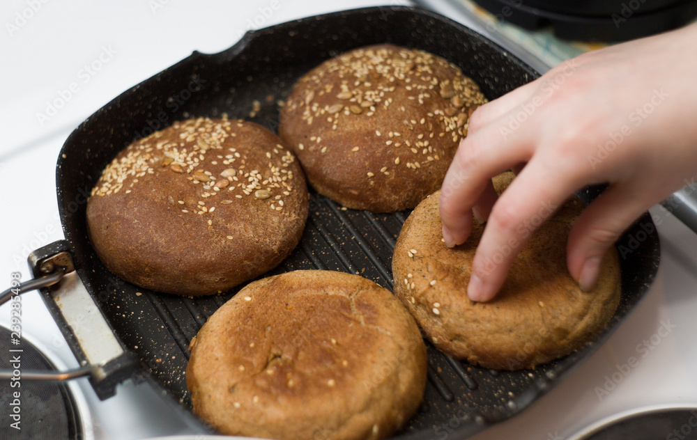 Fresh homemade buns for burgers, fried in a pan, the girl overturns them.