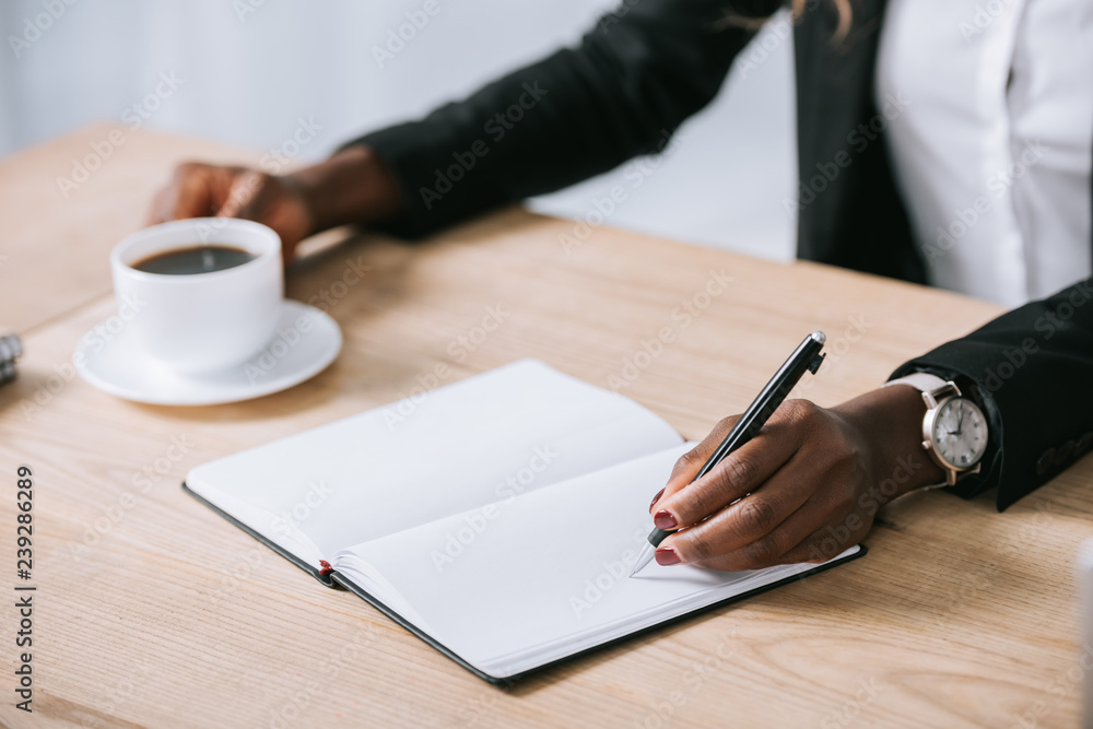 cropped view of african american woman with notebook and cup of coffee cropped view of african american woman with notebook and cup of coffee