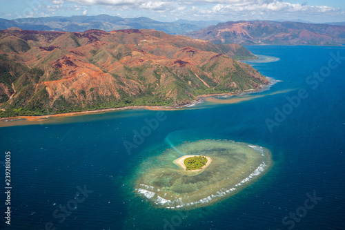 A small atoll islet with heart shaped coral reef off the east coast of Grande Terre island of New Caledonia, French overseas collectivity. Red green mountains hills full of nickel ore near Nakety. photo