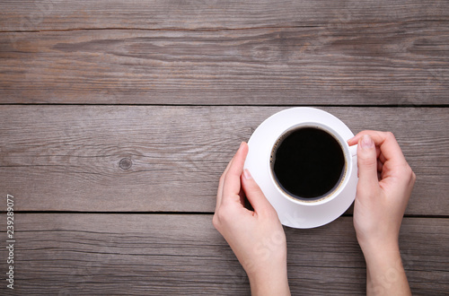 Female hands holding cup of coffee on grey wooden background.