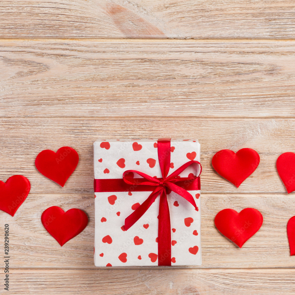 Valentine or other holiday handmade present in paper with red hearts and gifts box in holiday wrapper. Present box of gift on orange wooden table top view with copy space, empty space for design Valentine or other holiday handmade present in paper with red hearts and gifts box in holiday wrapper. Present box of gift on orange wooden table top view with copy space, empty space for design