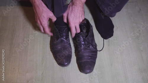 Man putting on and lacing up old shoes on the floor