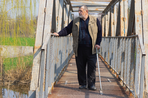 Senior man with walking stick standing on an metal bridge over small river