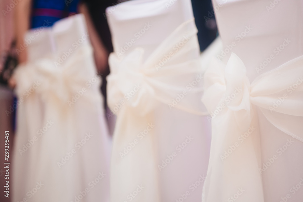 Decorated chairs. Silk bow tied on back of chair in party at restaurant. Wedding chair covers in white Decorated chairs. Silk bow tied on back of chair in party at restaurant. Wedding chair covers in white