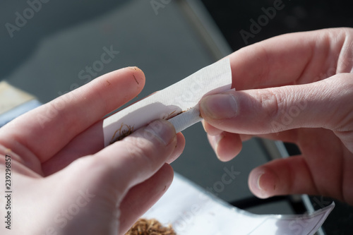 2 Hände drehen mit den Fingern, Tabak und Papier gekonnt eine selbstgedrehte Zigarette