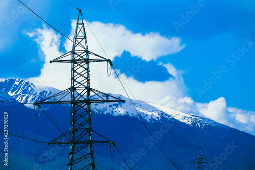 High-voltage powerful electricity tower with wires, alpine ice mountains peaks  on background.