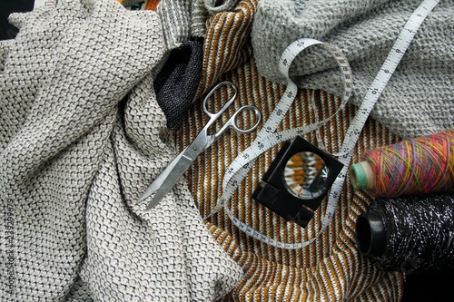 Background of bobbin, scissors, rule, magnifier with yarn and knitted fabric.