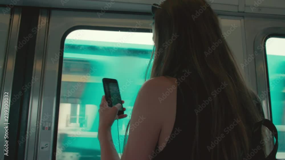 Beautiful young girl traveling in Paris passes time on the train by listening to music and taking pictures on her smartphone or mobile phone Beautiful young girl traveling in Paris passes time on the train by listening to music and taking pictures on her smartphone or mobile phone