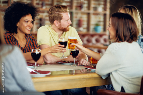 Friends making a toast while sitting in restaurant. Multi-ethnic group.