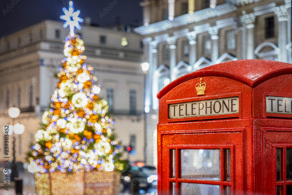 Naklejka premium Czerwona budka telefoniczna przed oświetloną choinką w Londynie w czasie świąt Bożego Narodzenia