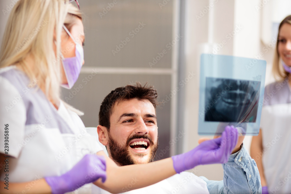 Young female dentist showing an x-ray image to a happy young male patient. Health care and medicine concept.