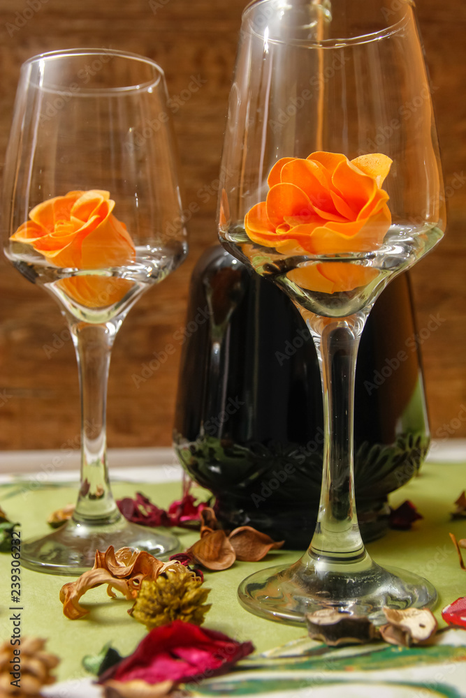 Romantic composition with wine glass, roses and bottle of wine. Candle light and dry leaves of flower on the table.