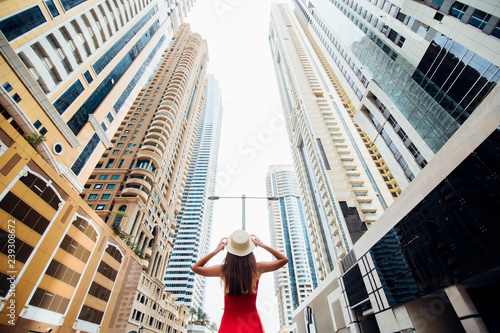Photography Young pretty woman in red dress and straw hat walking beetween skycrapers in modern city