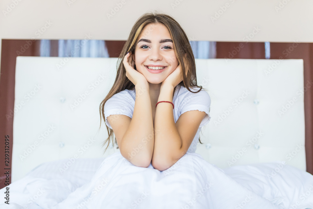 Positive woman sitting in bed and smiling to camera at home Positive woman sitting in bed and smiling to camera at home