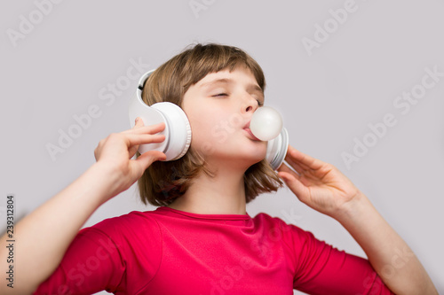 Little girl with headphones chewing gum on white