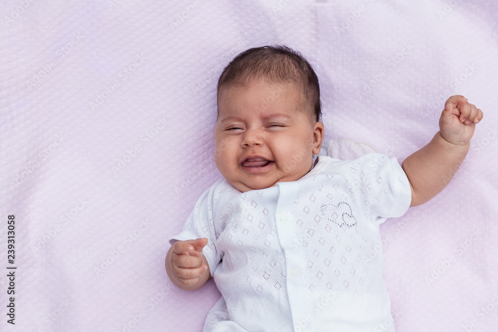 The baby lies on a pink background with a raised hand and crossed fingers, shows a bright emotion, copyspase The baby lies on a pink background with a raised hand and crossed fingers, shows a bright emotion, copyspase