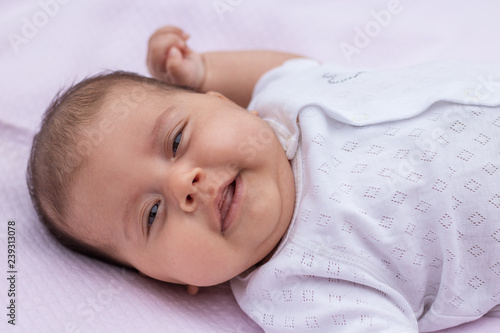 The baby lies on a pink background with a raised hand and crossed fingers, shows a bright emotion.