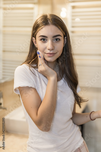 Beautiful young woman cleaning her face with sponge and smiling in bathroom