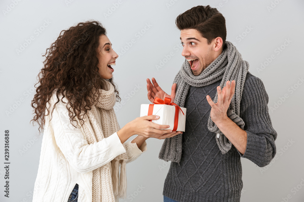 Image of pleased man and woman rejoicing while standing with present box, isolated over gray background