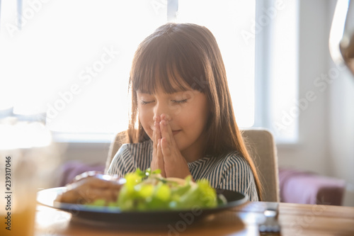 Little girl praying before meal at home photo