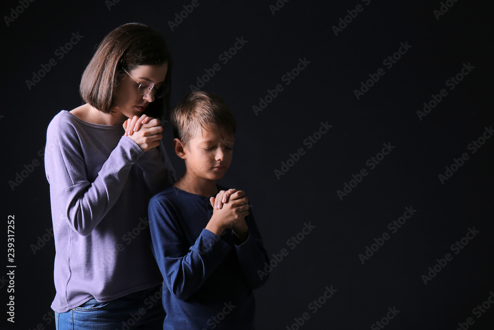 Praying mother and son on dark background Praying mother and son on dark background