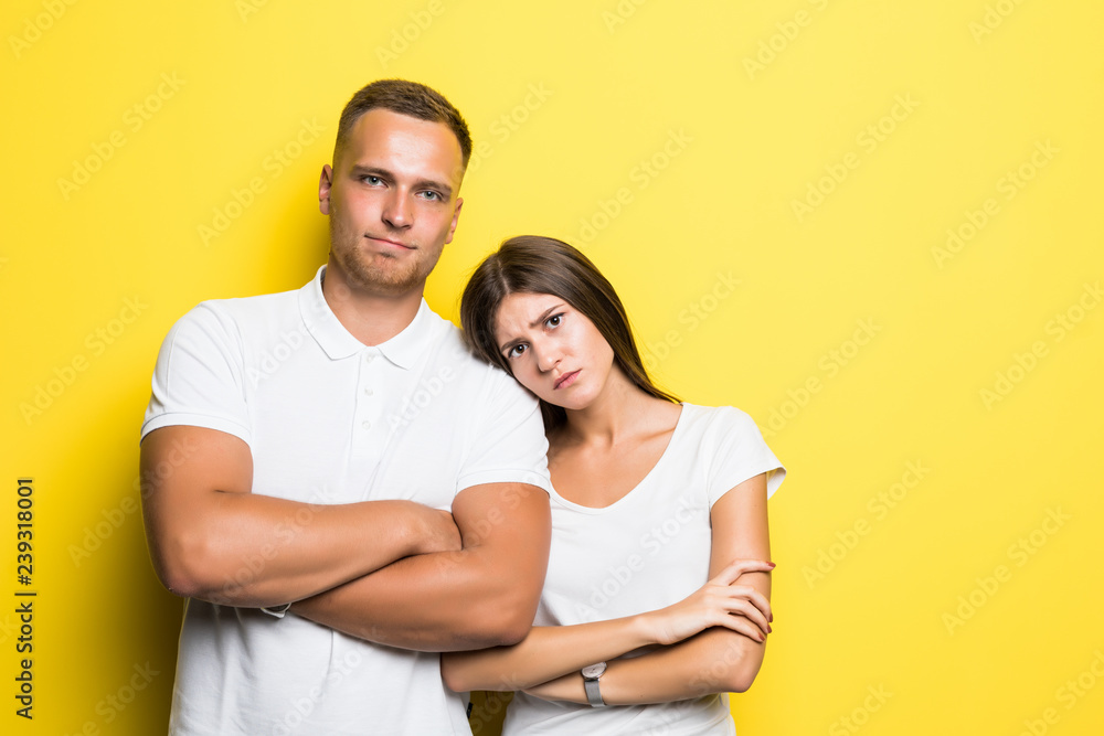 Portrait of content young couple in basic clothing smiling at camera while woman putting her head on male shoulder isolated over yellow background Portrait of content young couple in basic clothing smiling at camera while woman putting her head on male shoulder isolated over yellow background