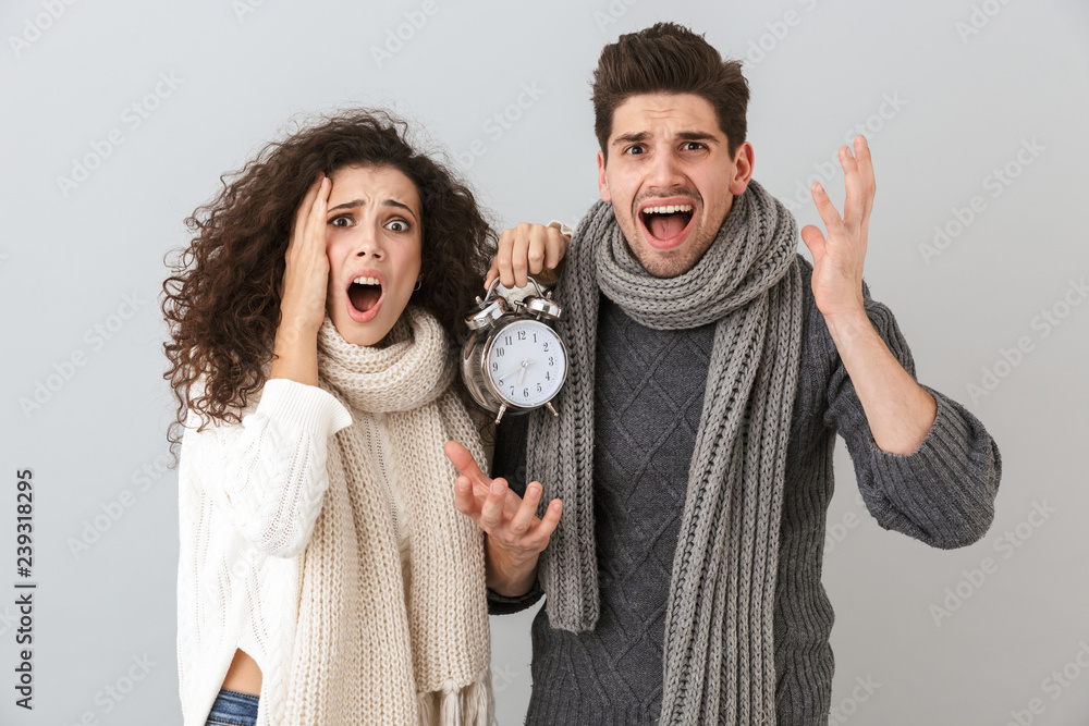Image of upset couple man and woman screaming while holding alarm clock, isolated over gray background Image of upset couple man and woman screaming while holding alarm clock, isolated over gray background