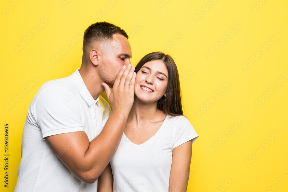 Portrait of handsome man whispering secret or interesting gossip to young woman in her ear isolated over yellow background Portrait of handsome man whispering secret or interesting gossip to young woman in her ear isolated over yellow background