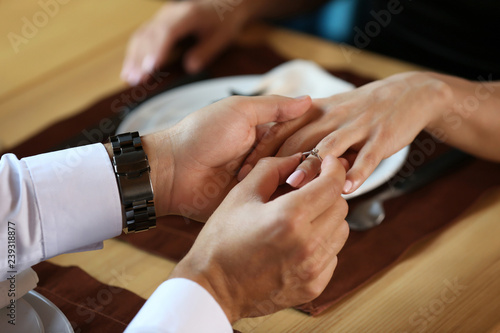 Young man putting engagement ring on fiancee s finger in restaurant