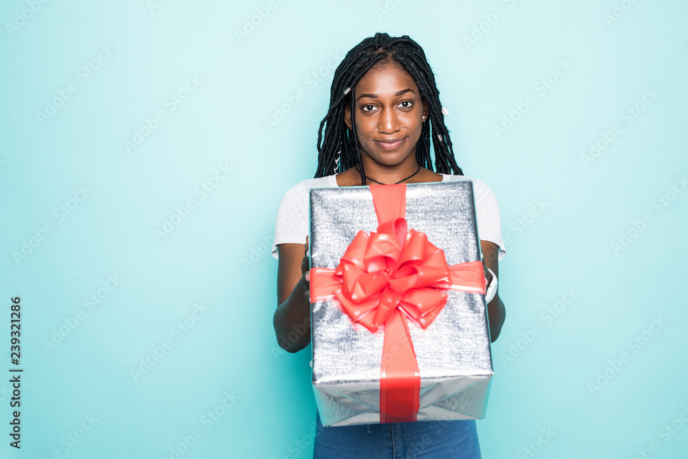 Portrait of joyous african woman with afro hairdo holding gift box and smiling in happiness over blue background Portrait of joyous african woman with afro hairdo holding gift box and smiling in happiness over blue background