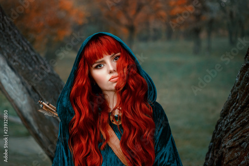 attractive red-haired girl looking at the camera with brown eyes, wearing blue velor velvet cloak with hood on her head, has leather quiver for arrows, warrior bravely looks into the eyes of death