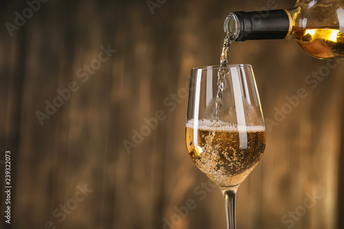Bilde på lerret Pouring of white wine from bottle into glass on dark background