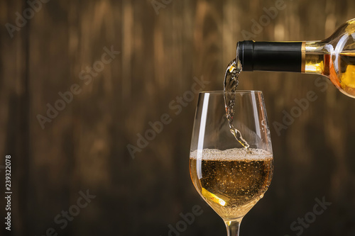Pouring of white wine from bottle into glass on dark background photo