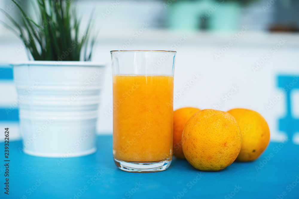 A fresh orange juice with some oranges nearby placed on a blue table with a table plant A fresh orange juice with some oranges nearby placed on a blue table with a table plant