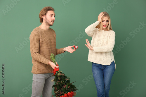 Young woman rejecting marriage proposal on color background photo