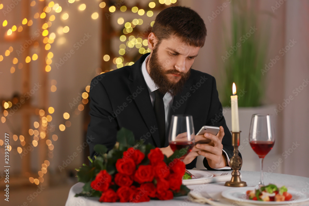 Young man with mobile phone waiting for his girlfriend in restaurant Young man with mobile phone waiting for his girlfriend in restaurant