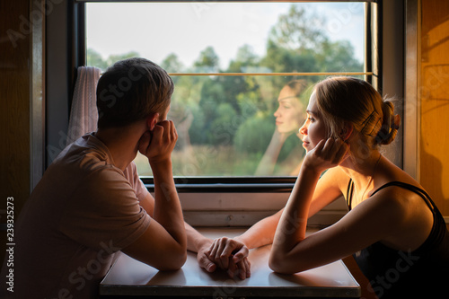 Couple of lovers traveling in train. Mood portrait of romantic pair in wagon looking at window with self reflections in it. Adventure on holiday of happy friends. Man and woman looking at each other.