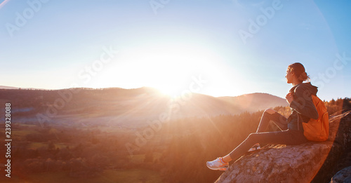 woman sits on edge of cliff against background of sunrise