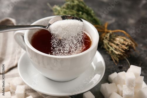 Adding of sugar to cup with aromatic tea on grey table