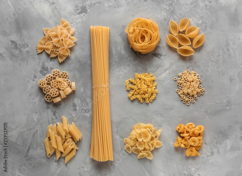 Different types of raw pasta on grey background