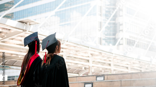 Two girls in black gowns standing look up to the sky with happy graduates.