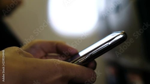 Man close-up is using a smartphone inside an airplane next to a window
