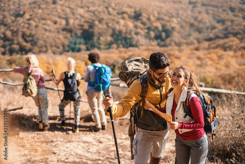 Cute couple looking at map while their friends in background looking at view. Hiking concept.