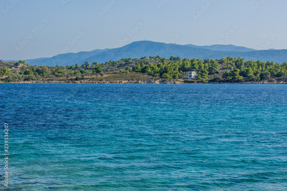 tropic Mediterranean sea beach with vivid blue water surface and small waves with view on opposite forest waterfront coast shoreline