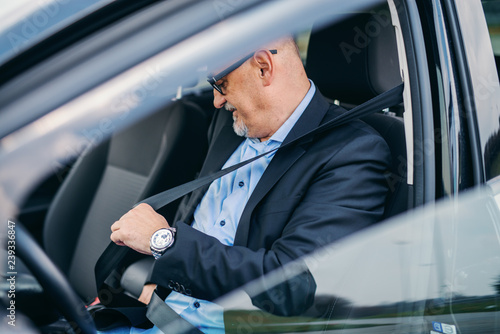 Bearded senior adult businessman fastening seat belt in his car. © dusanpetkovic1
