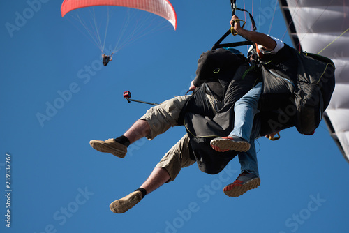 Dwie tandemowe paralotnie latają na tle błękitnego nieba, tandemowe paralotniarstwo prowadzone przez pilota