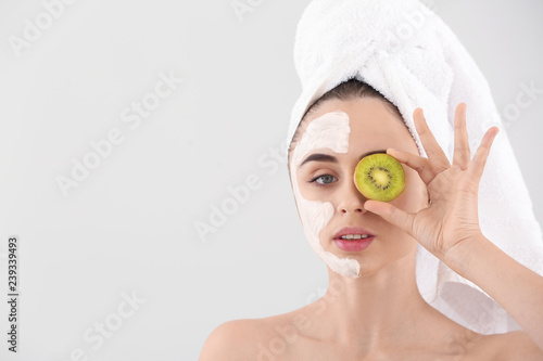 Beautiful young woman with kiwi facial mask on light background